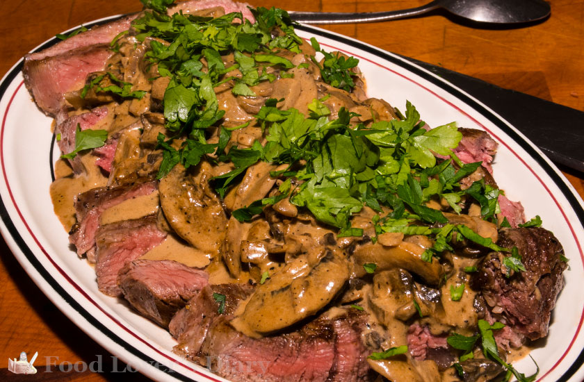 Ribeye sliced on plate covered with mushrooms and parsley